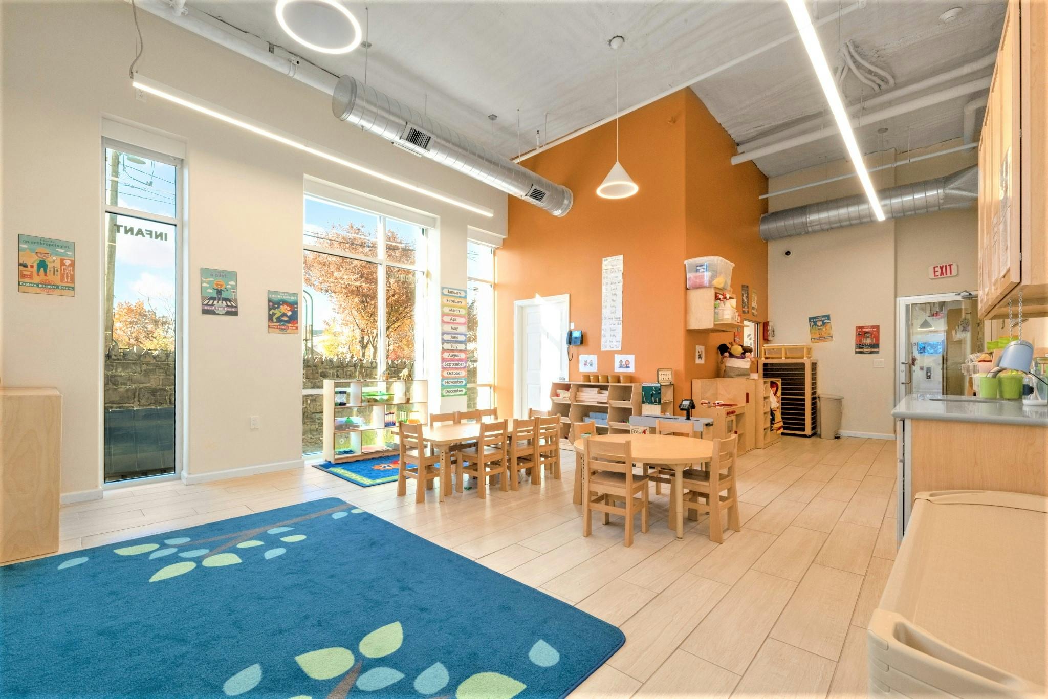 Classroom with small tables and chairs, a blue rug, and large windows