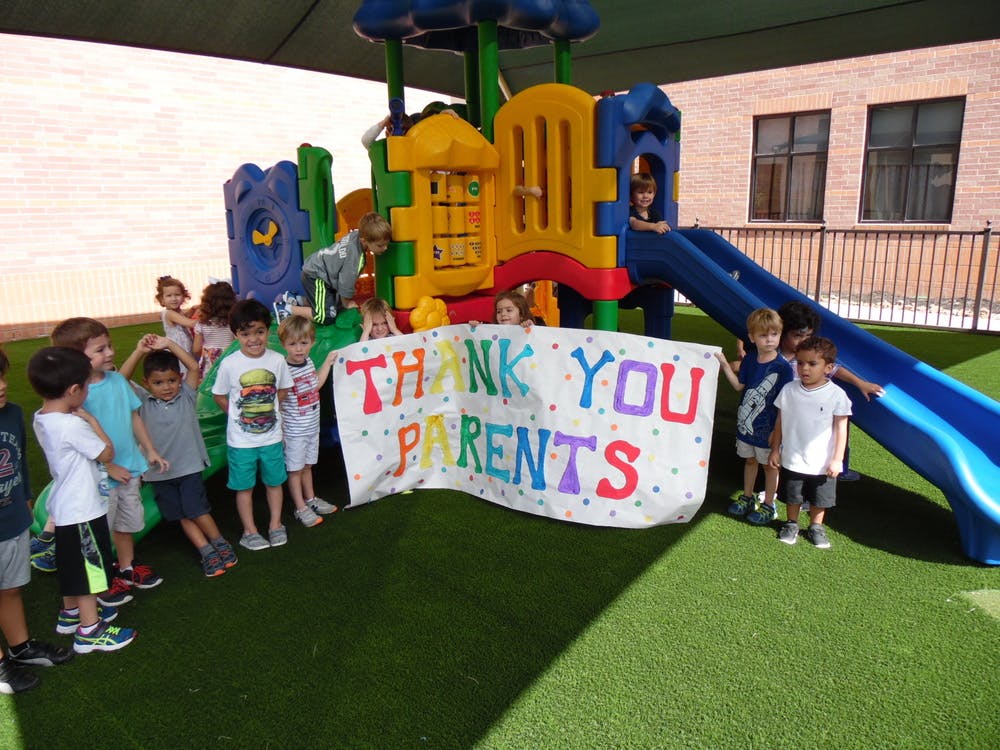 Children holding a banner that says "Thank You Parents" on a playground