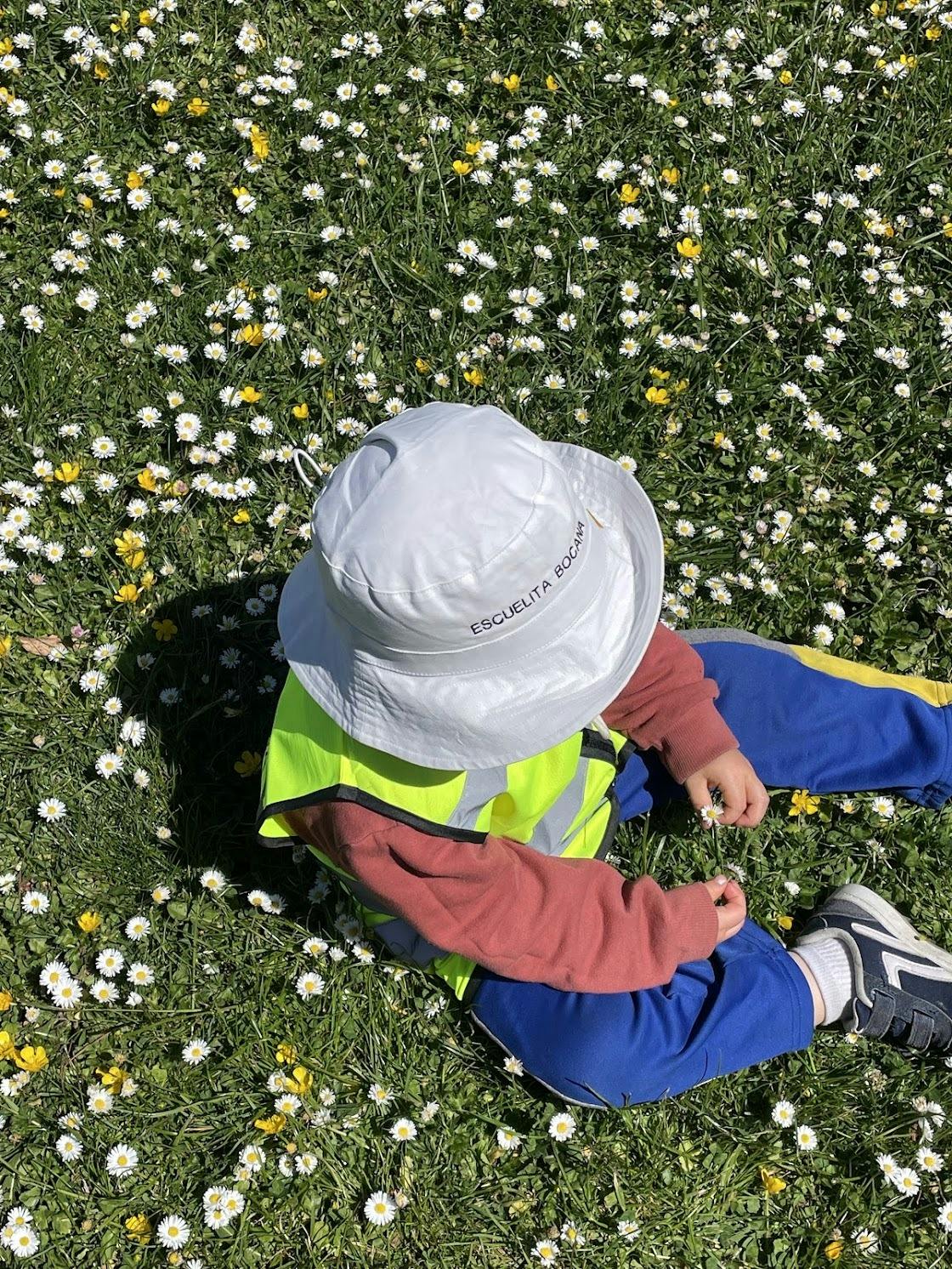 Child wearing a hat and high-visibility vest sitting in a field of flowers