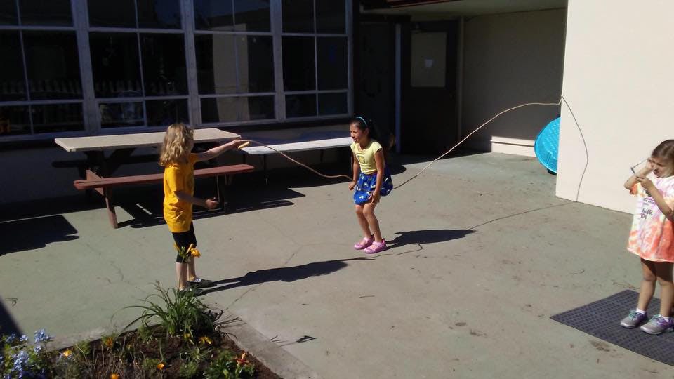 Three children playing with a jump rope outdoors
