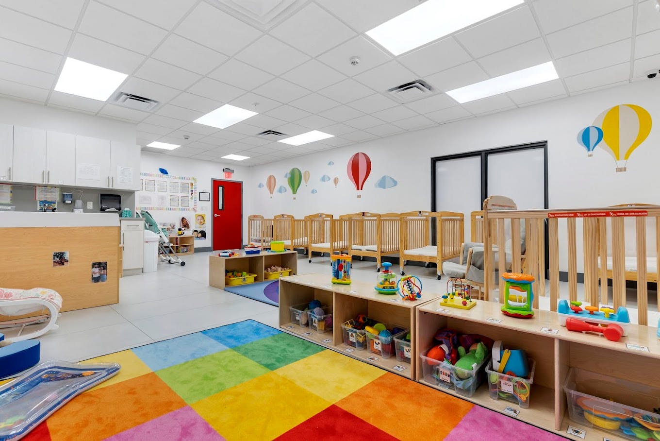 Daycare room with cribs, colorful rug, and shelves of toys