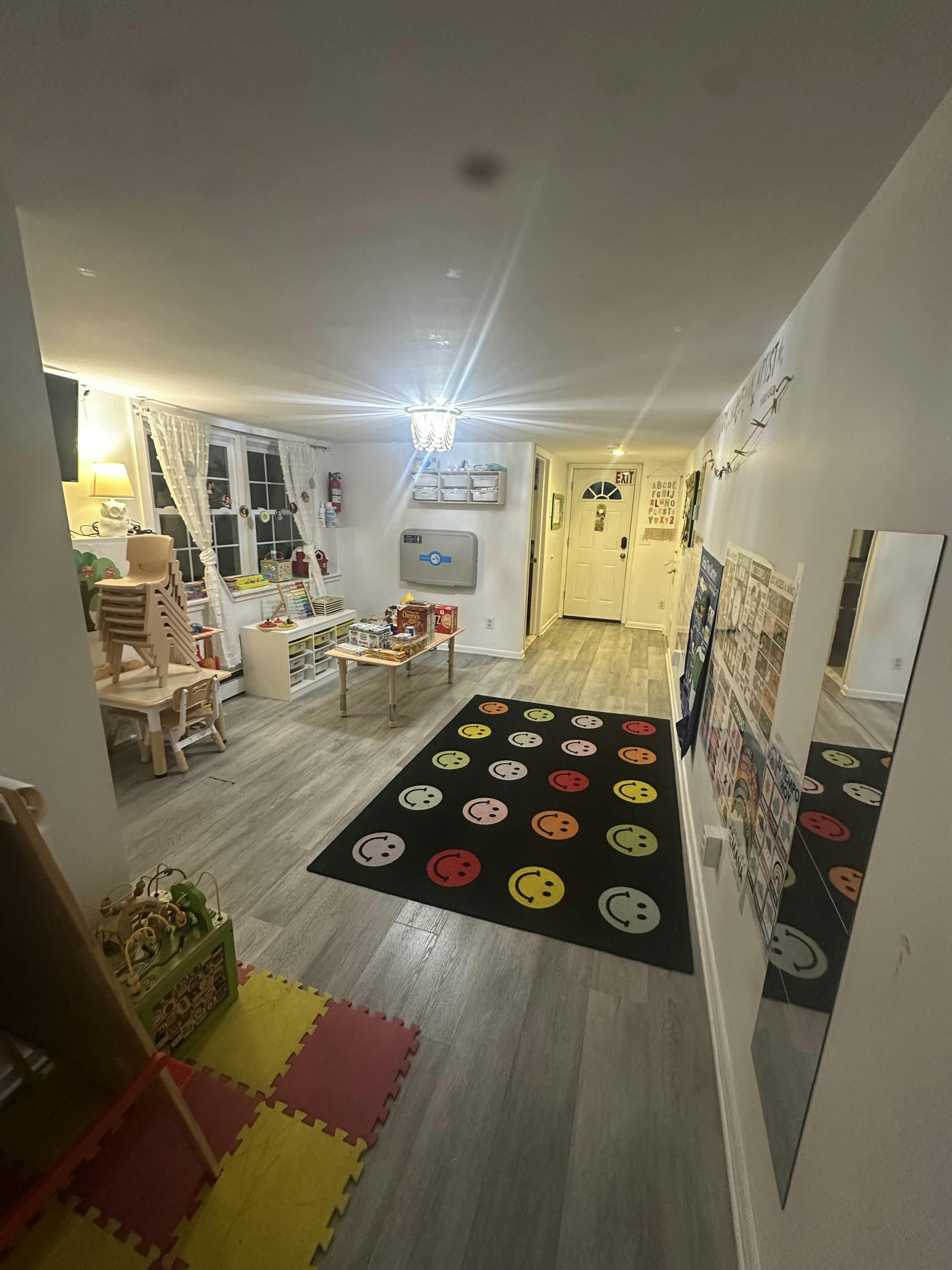 Children's play area with a colorful rug, small tables, chairs, and learning posters