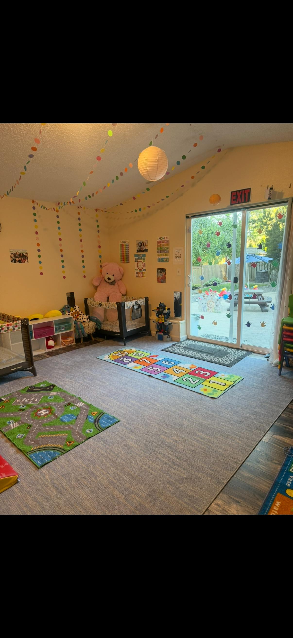 Playroom with play mats, toys, and a large teddy bear by a glass door
