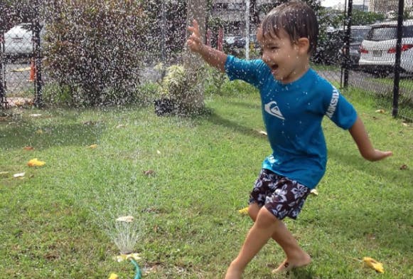 Child playing in a sprinkler on a grassy lawn
