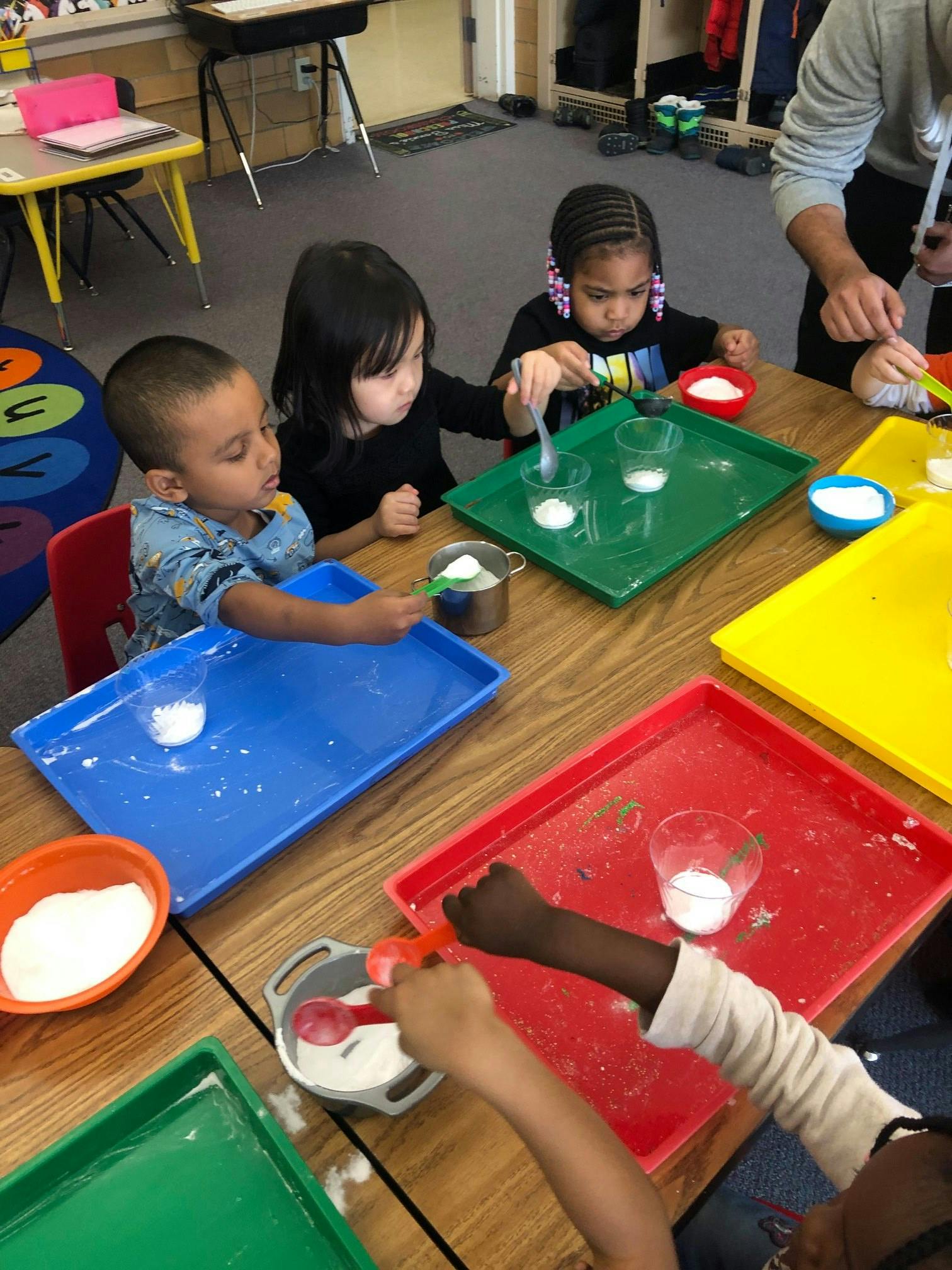 Children at a table with colorful trays and cups of white powder