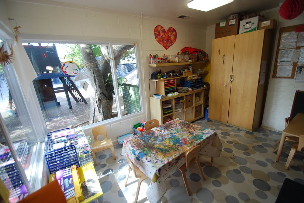 Classroom with a table covered in a colorful cloth, shelves, and a large window