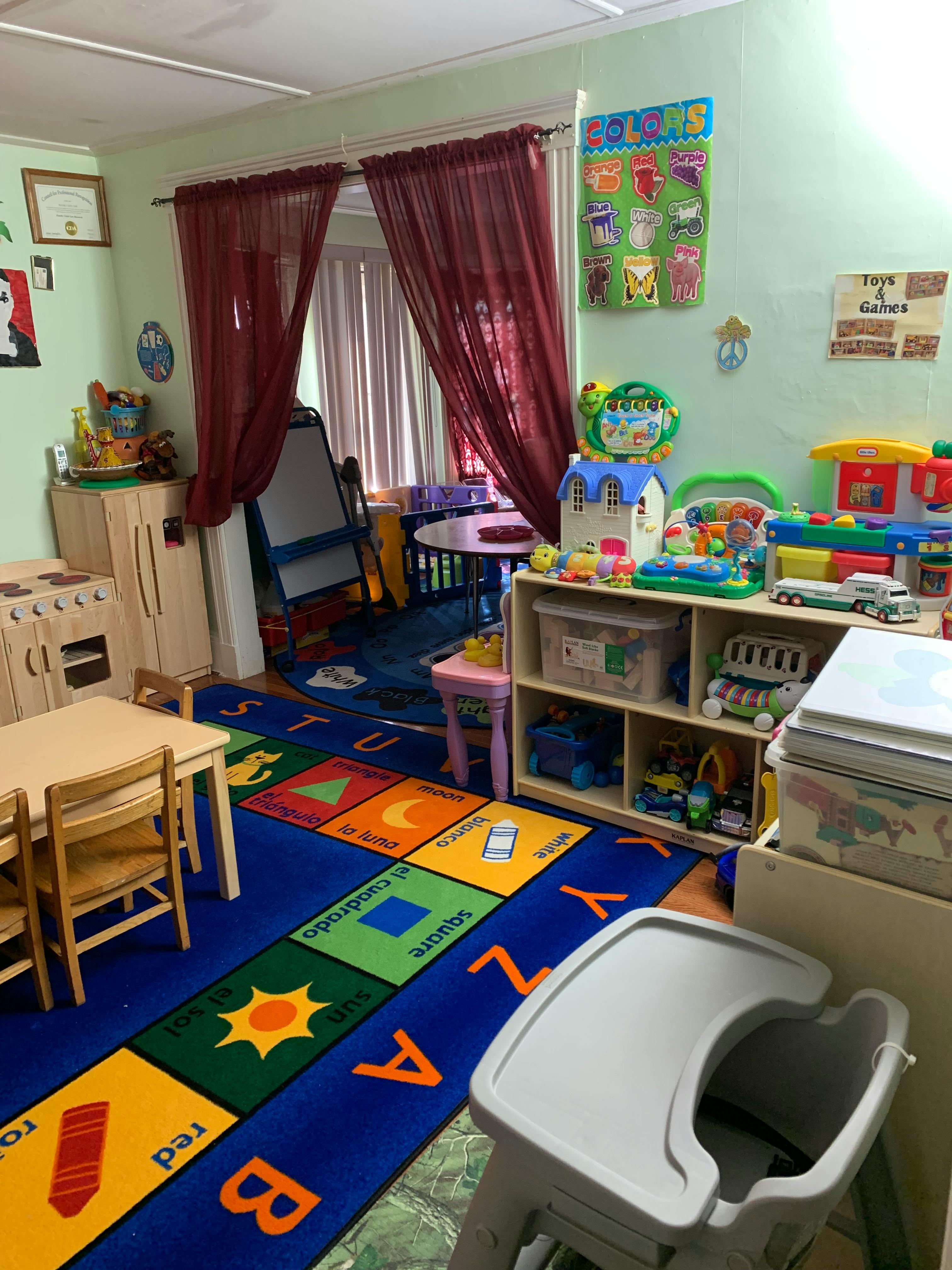 Classroom filled with toys, a high chair, and a rug with letters and shapes