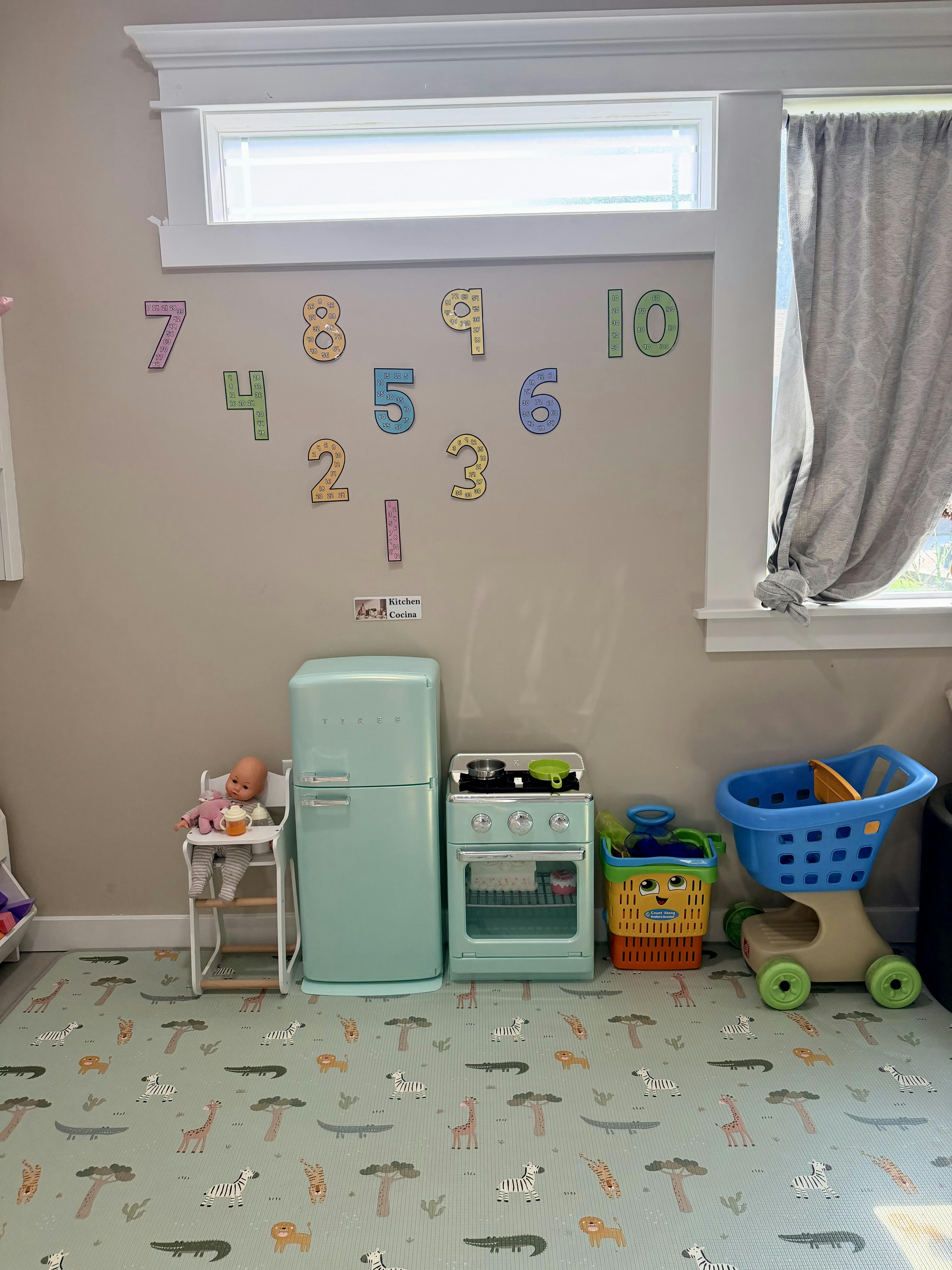 Play kitchen setup with toy appliances and shopping cart on a play mat