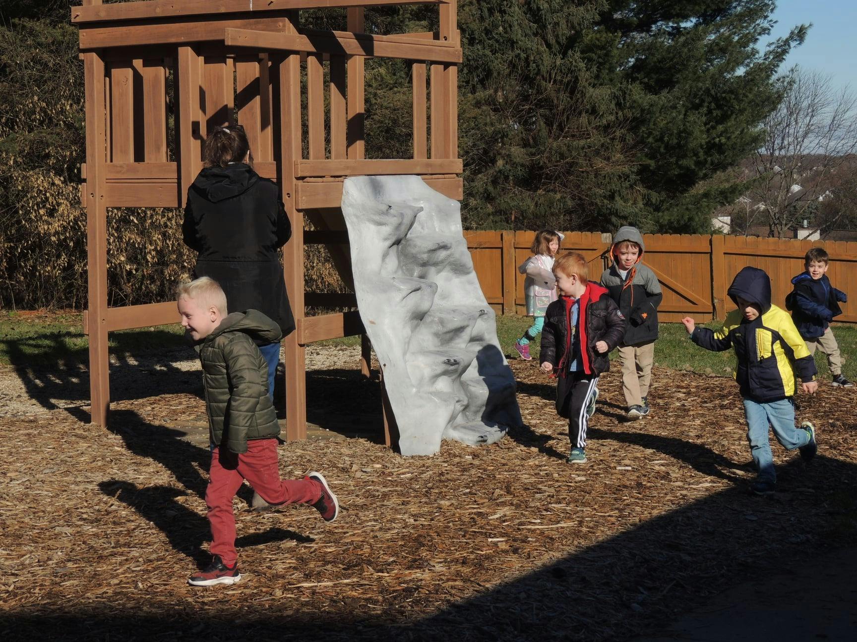 Children playing on a playground with a person standing near a wooden structure
