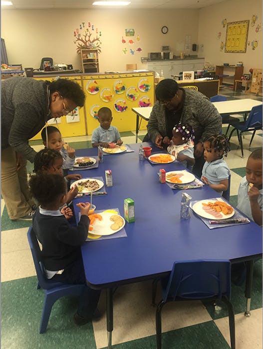 Adults and children eating at a table in a classroom