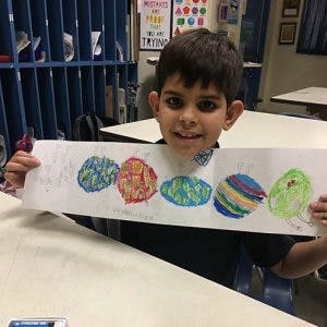 Child holding up a drawing of colorful planets