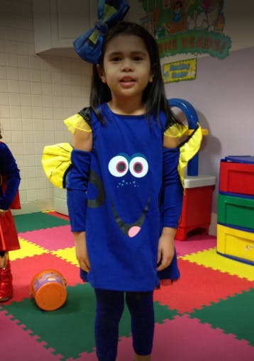 Child in a blue costume with large eyes and a bow on a colorful floor