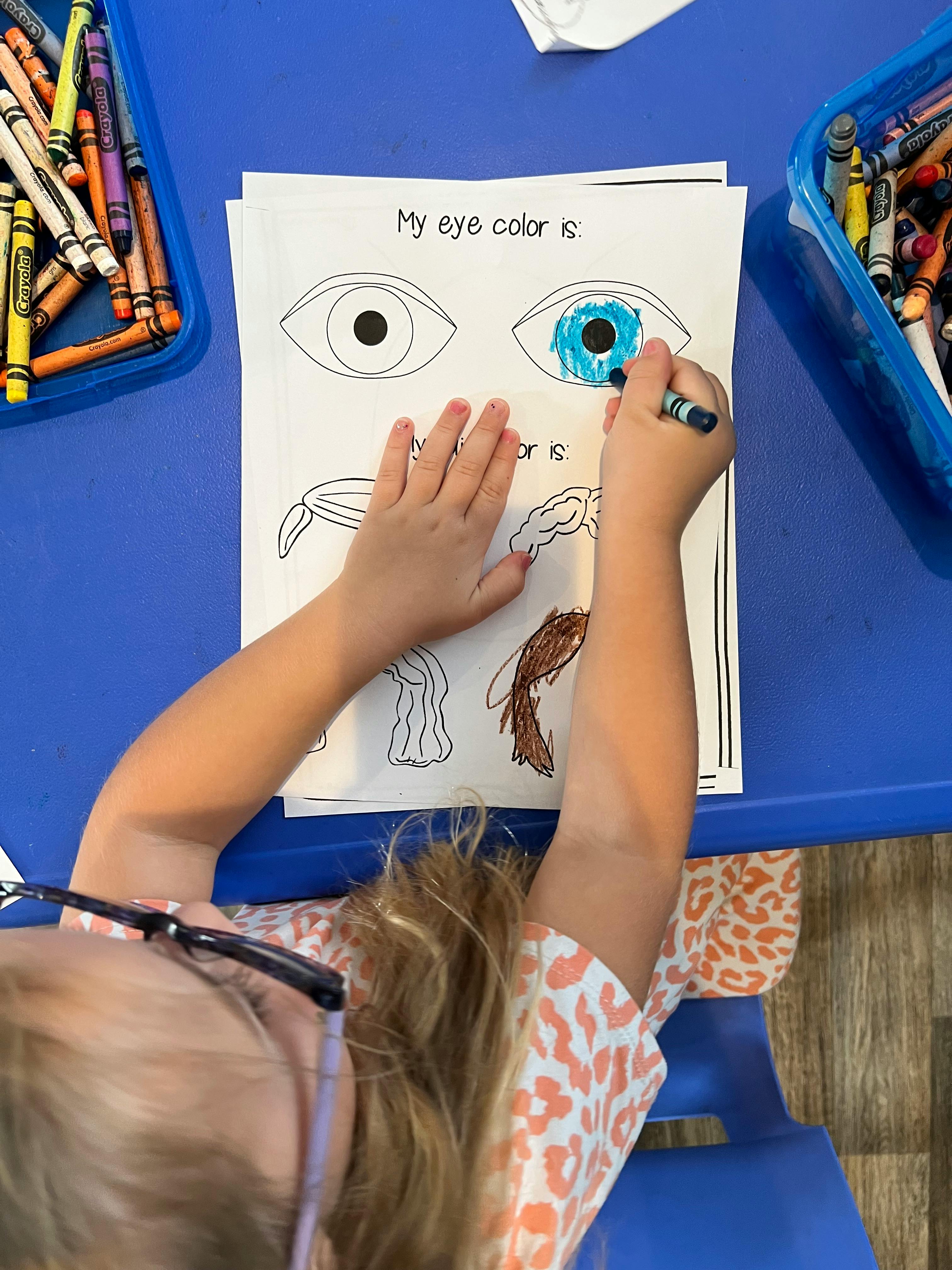 Child coloring an eye blue on a worksheet that says "My eye color is"