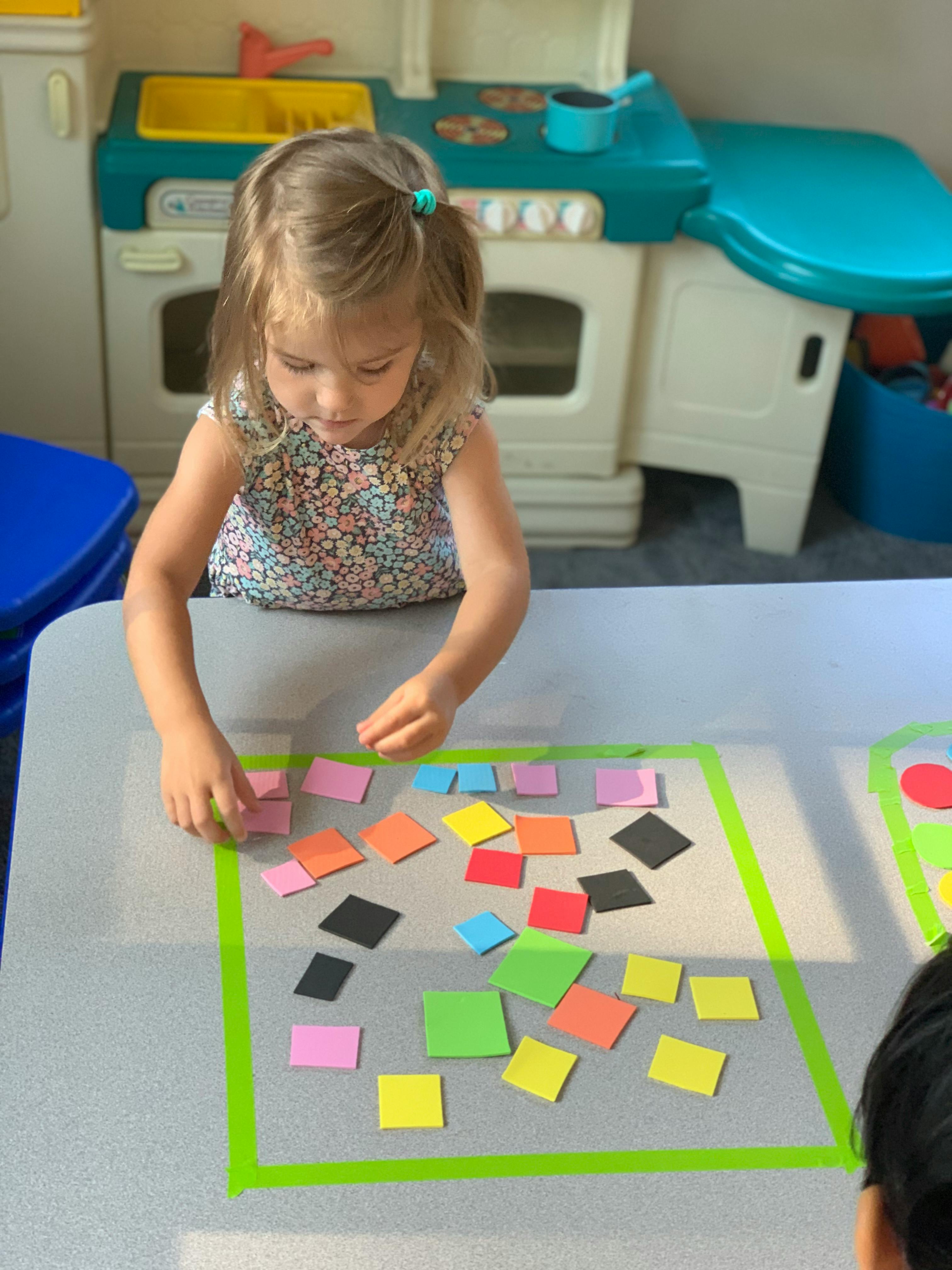 Child playing with colorful square cutouts on a table