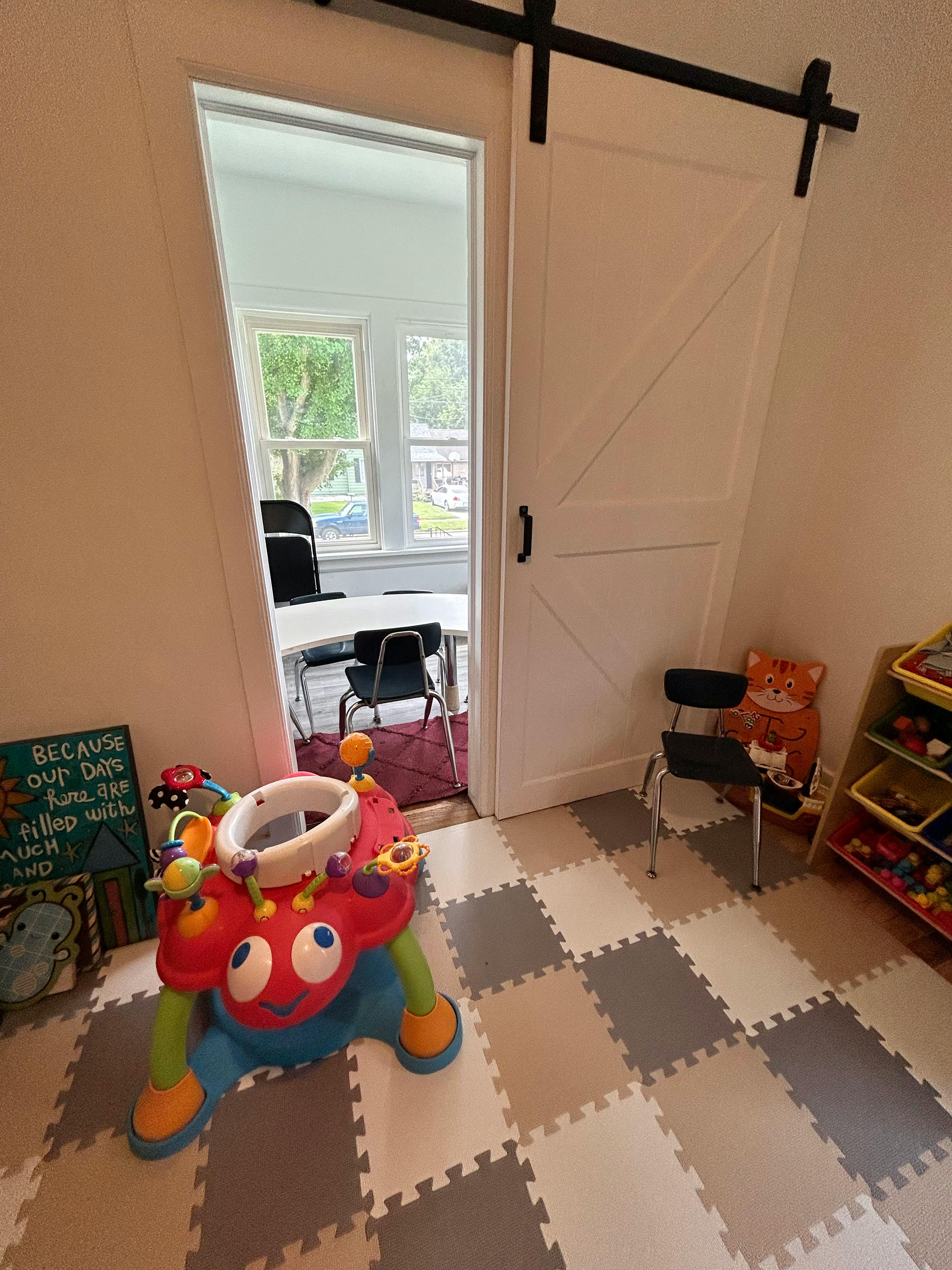 Baby activity center on a checkered floor with a partially open barn door