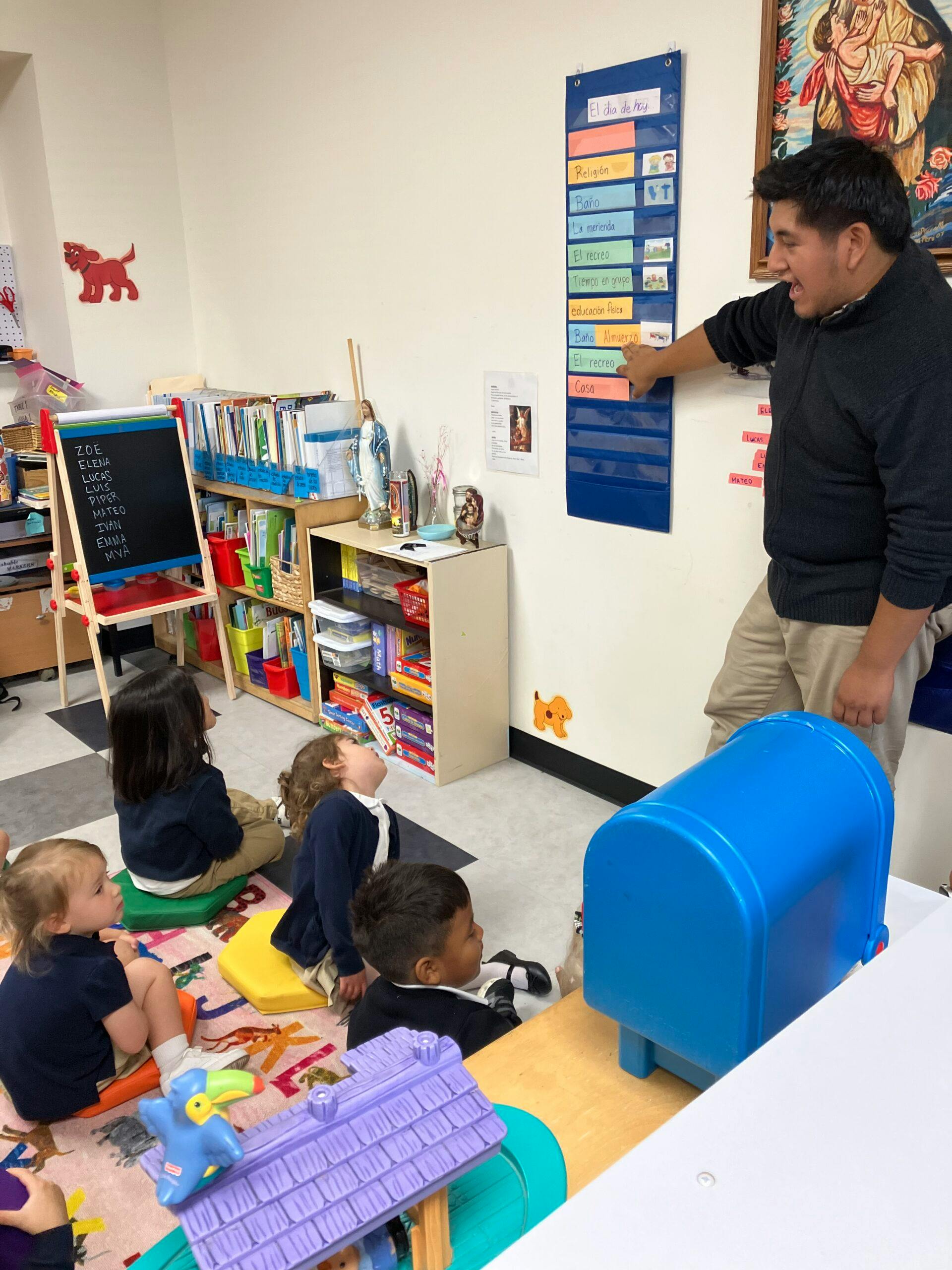 Teacher pointing to a schedule board with children sitting on the floor in a classroom