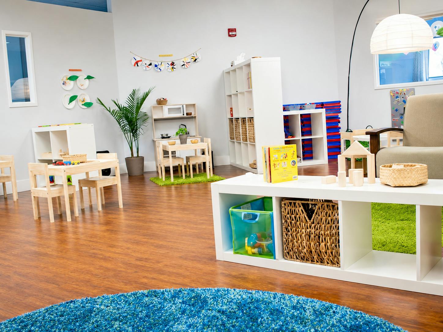 Childcare classroom with tables, chairs, and play equipment on wood flooring