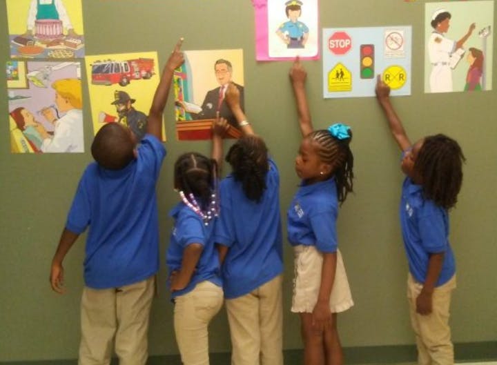 Four children in blue shirts pointing at pictures on a wall