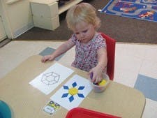 Child at a table with papers and a container of small objects