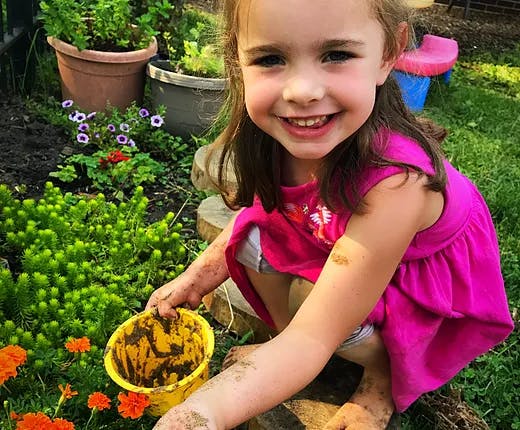 Child with muddy hands holding a yellow bucket in a garden