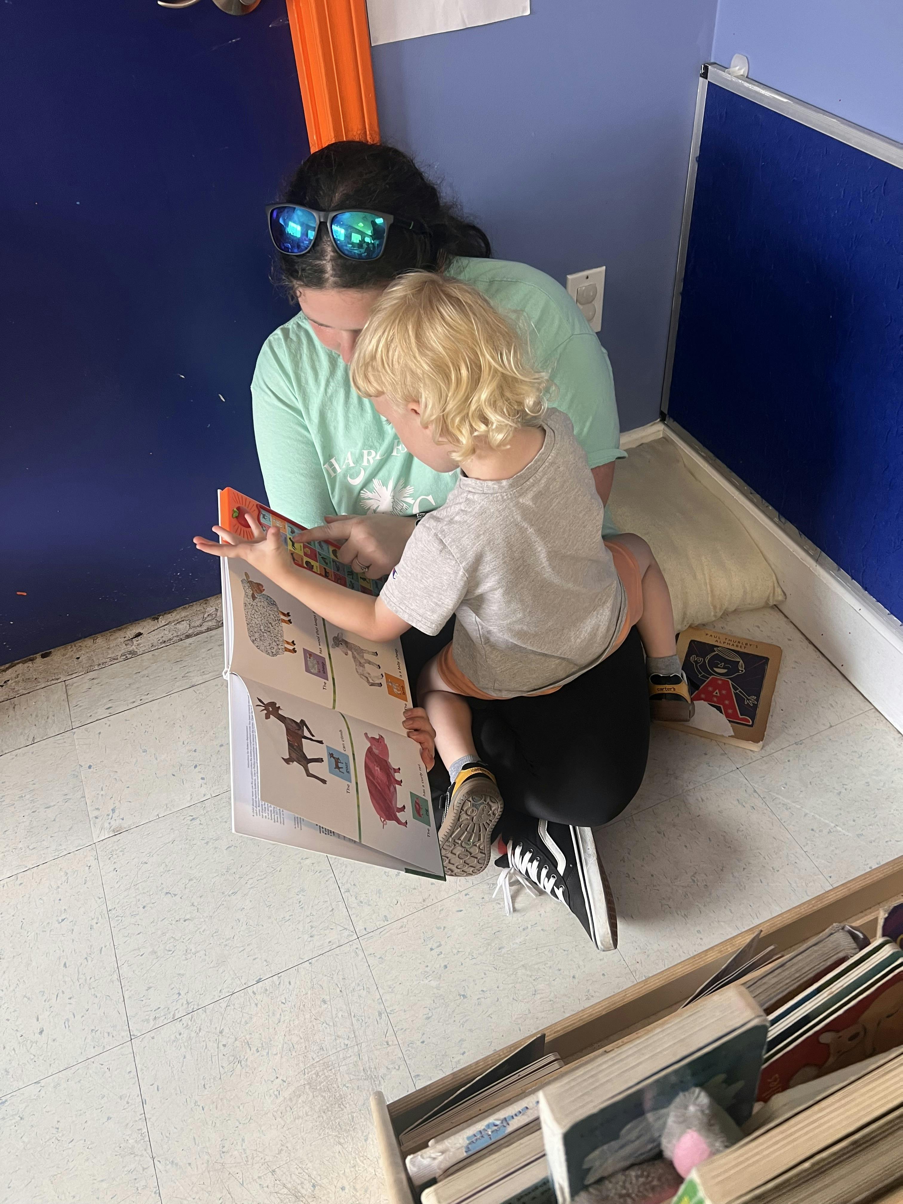 A person sitting on the floor reading a book to a child