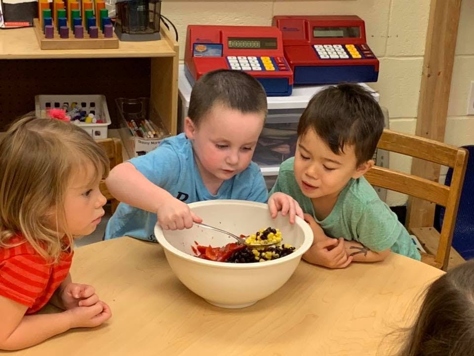 Three children mixing ingredients in a bowl at a table