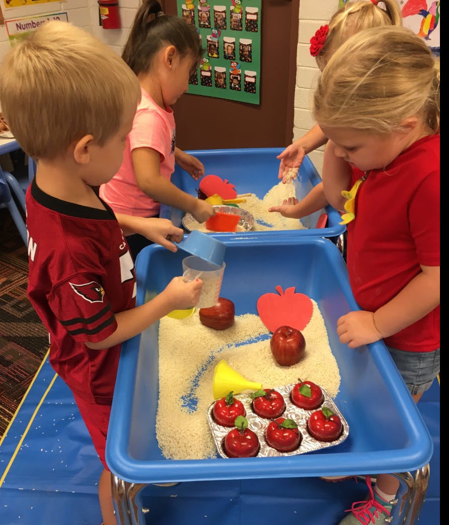 Children playing with rice and apple-themed toys in sensory bins