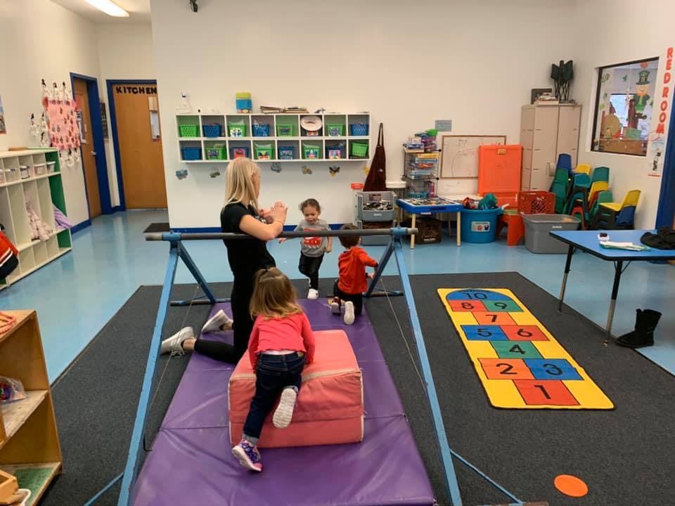 Adult and children playing on gymnastics equipment in a classroom