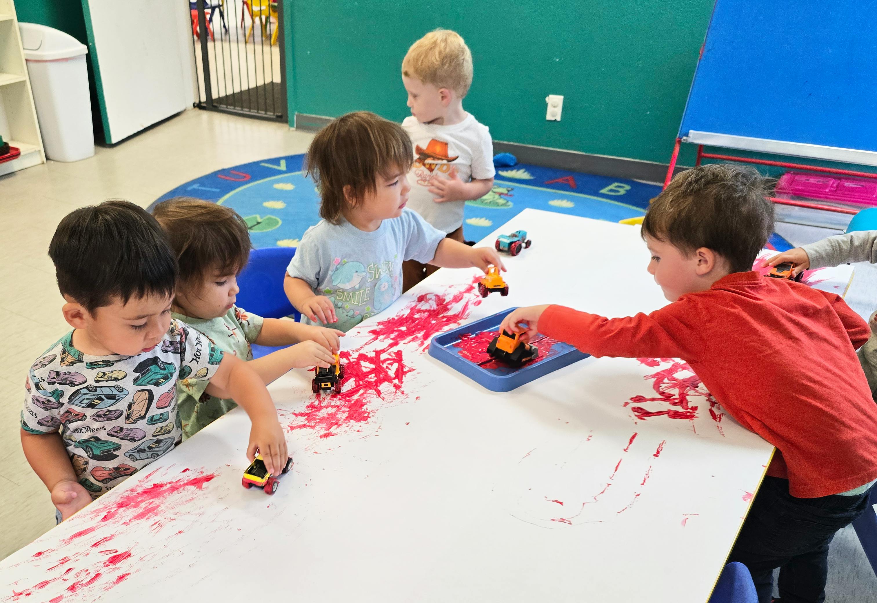 Children painting on a table using toy vehicles
