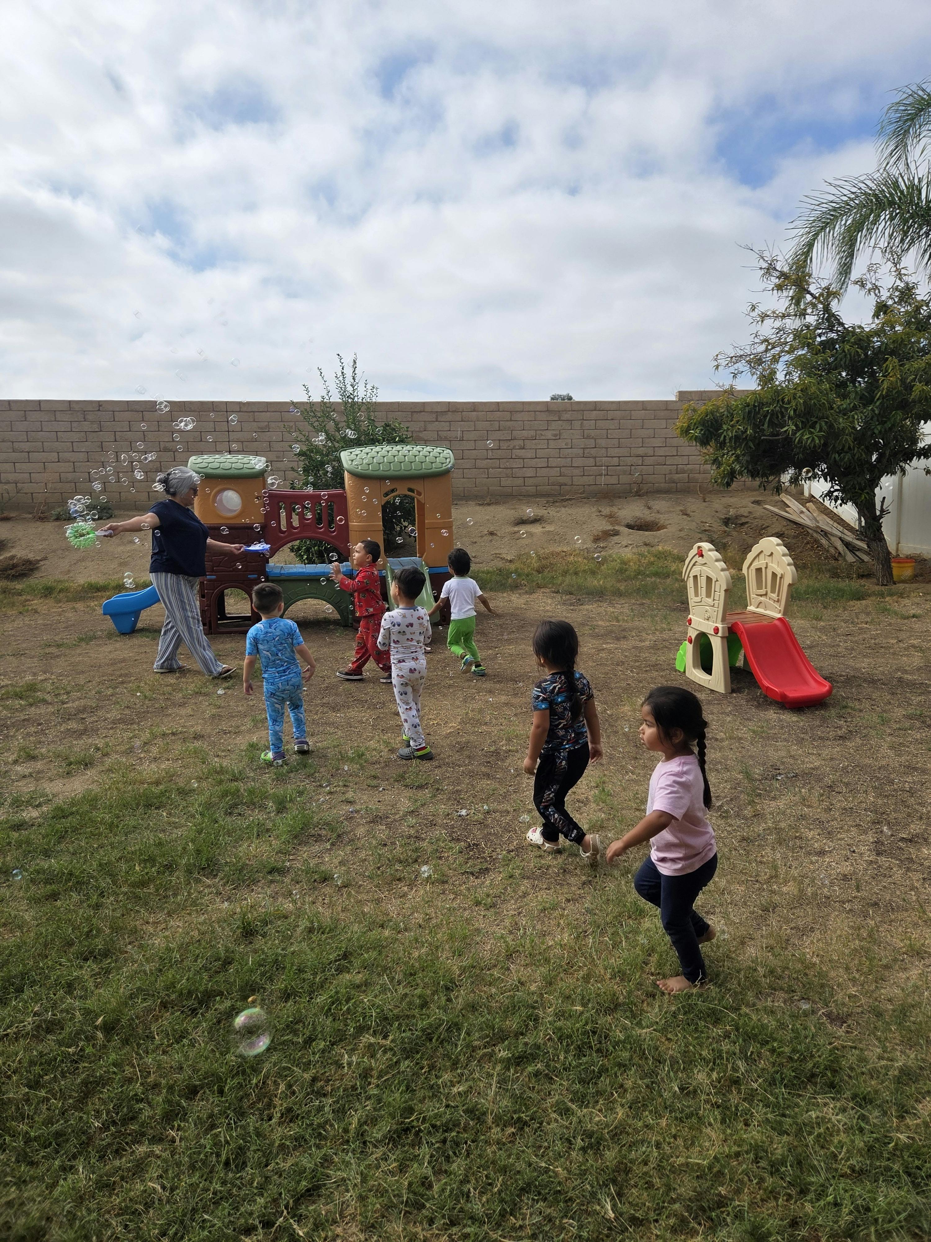 Adult and children playing with bubbles in a yard with playground equipment
