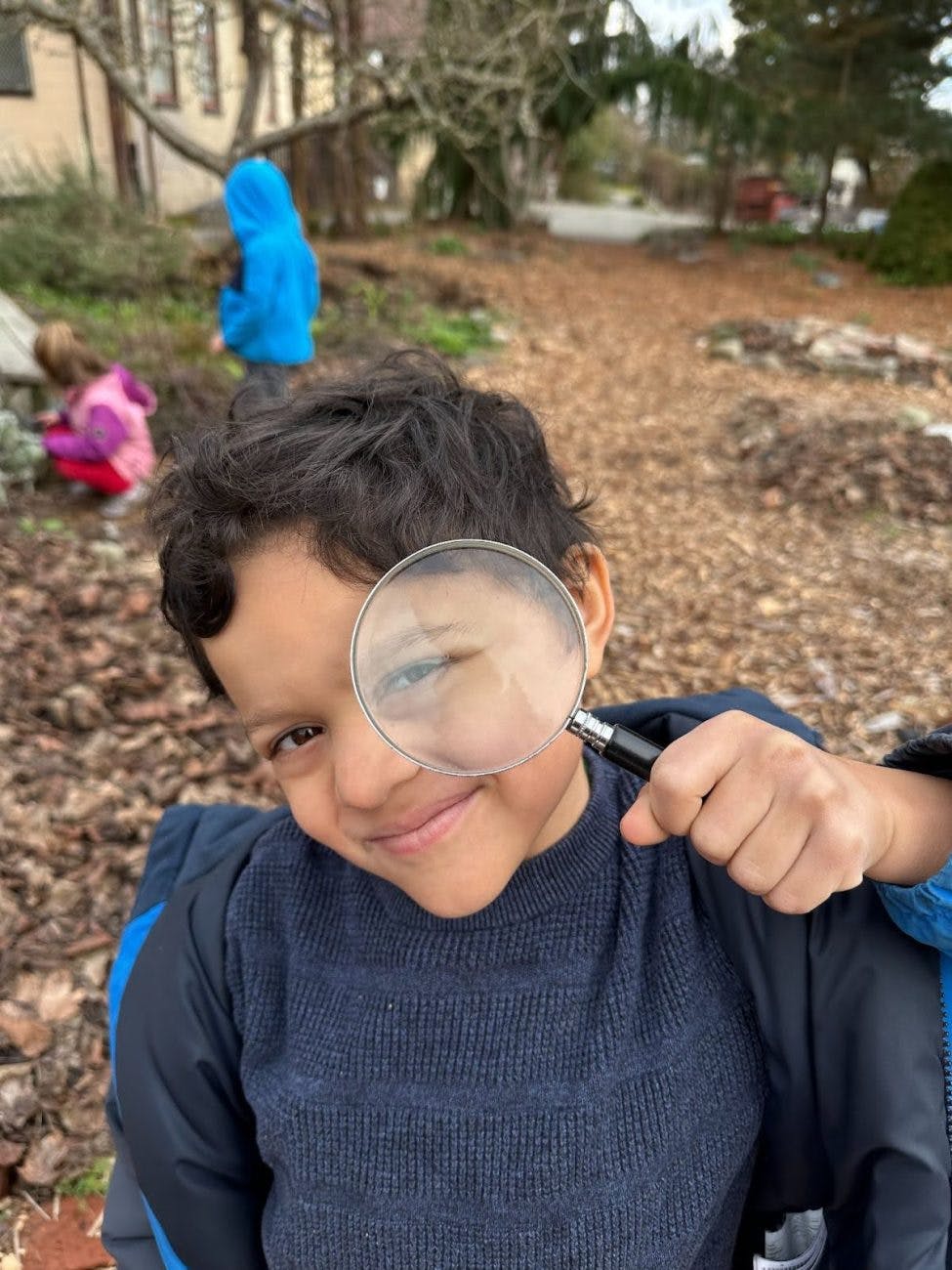 Child in blue sweater holding magnifying glass over one eye