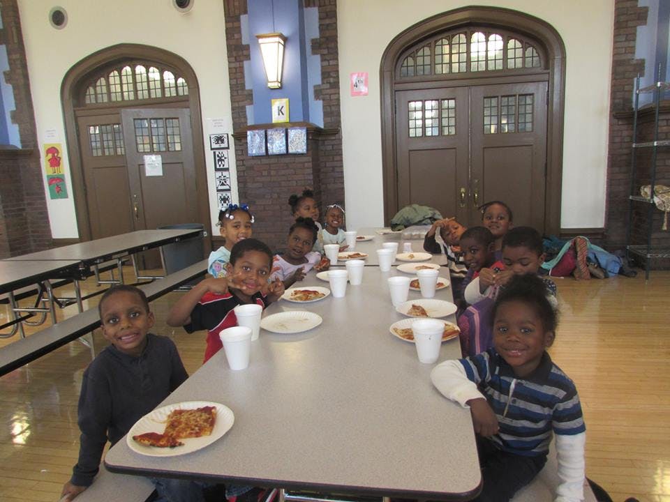 Children sitting at a long table with plates of food and cups