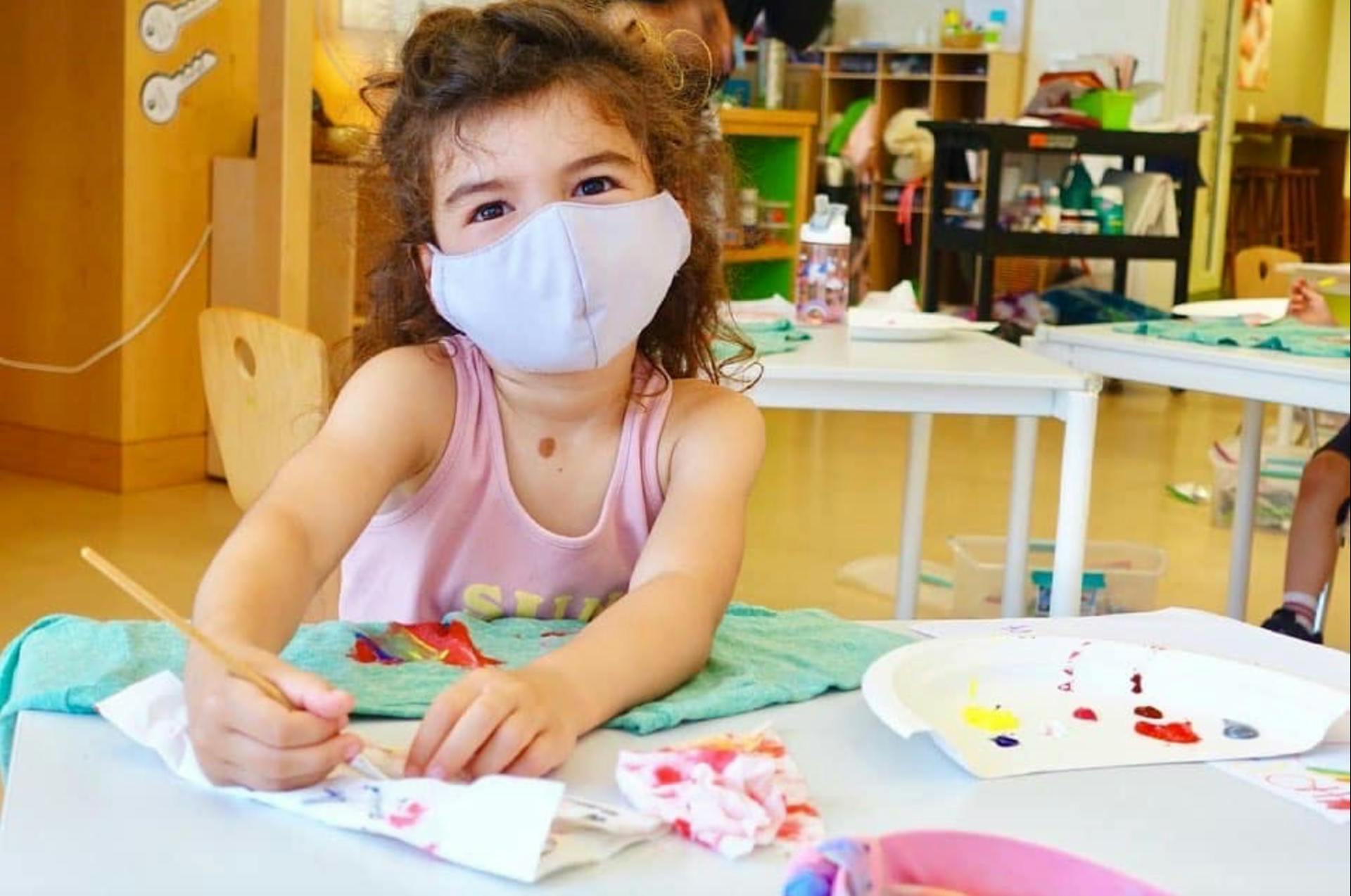 Child in a mask painting in a classroom