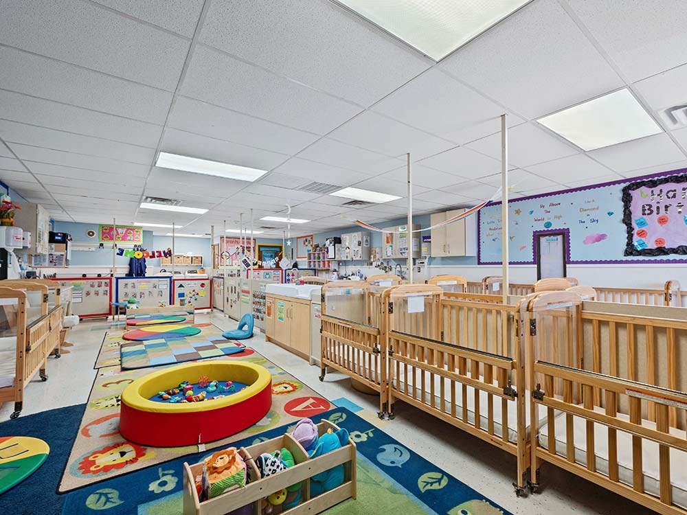 A colorful childcare room with cribs, play mats, and a ball pit