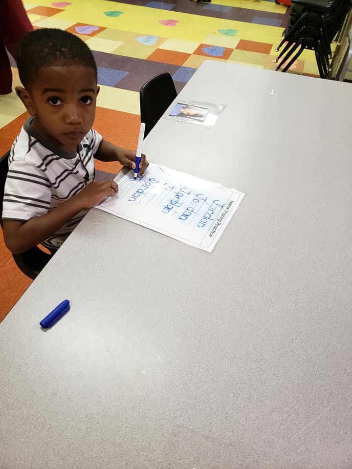 Child writing on paper at a table in a classroom