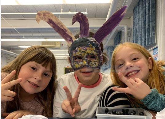 Three children making peace signs, one wearing a mask with bunny ears