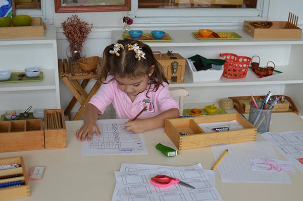 Child writing on paper at a desk in a classroom