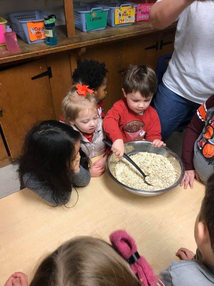 Children gathered around a bowl of oats with a spoon