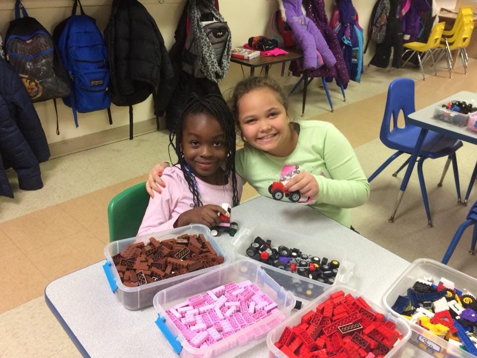 Two children sitting at a table with plastic bins of building blocks