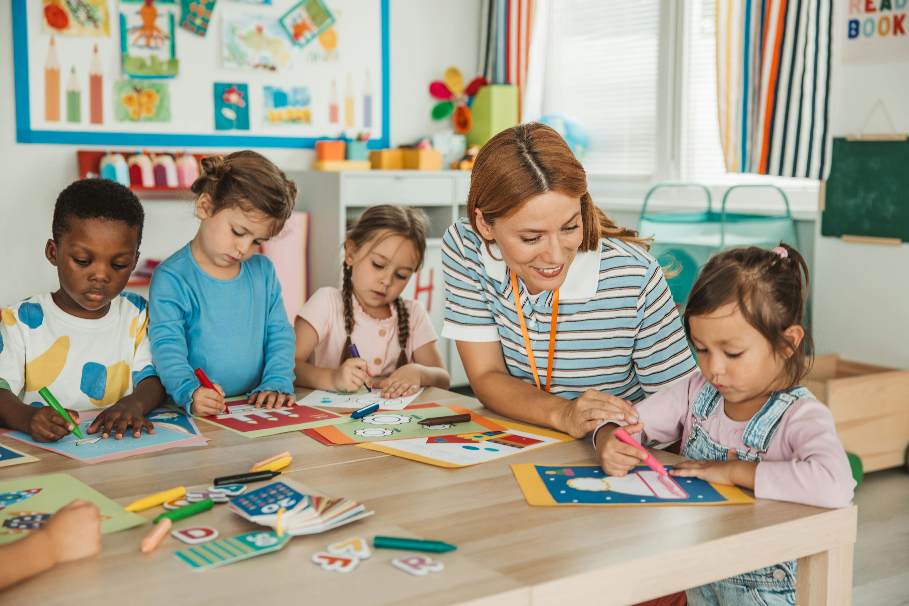 Five children and an adult person coloring at a table in a classroom