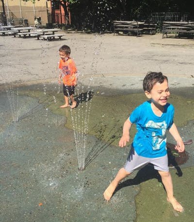 Two children playing in water from ground sprinklers