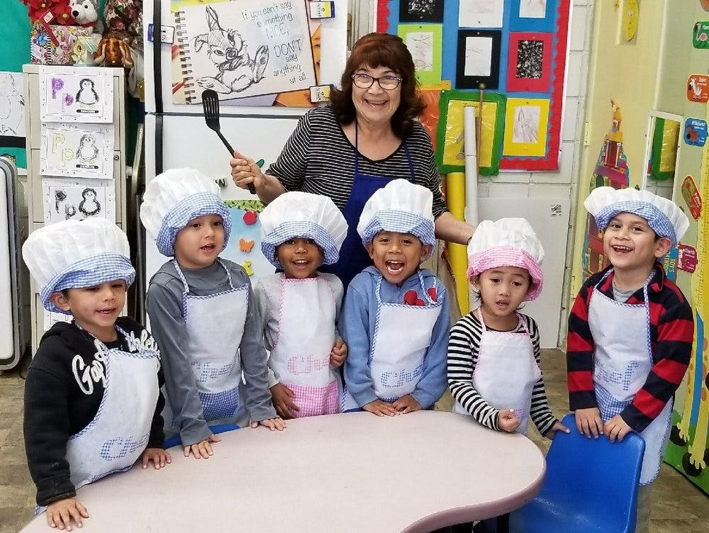 Adult and five children wearing chef hats and aprons in a classroom