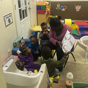 Adult reading a book to four children in a classroom
