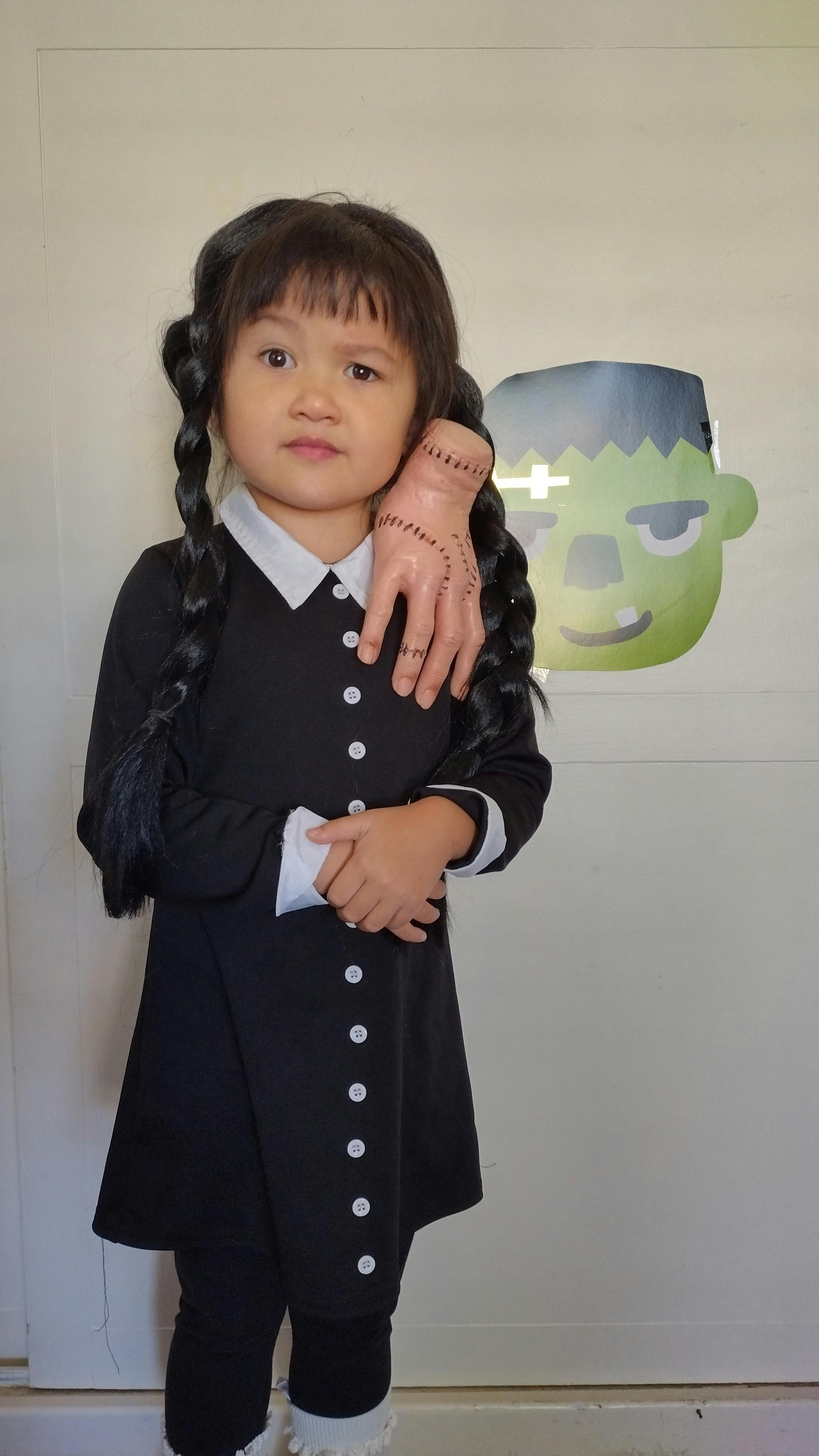 Child in a black dress with braided hair and a toy hand on their shoulder