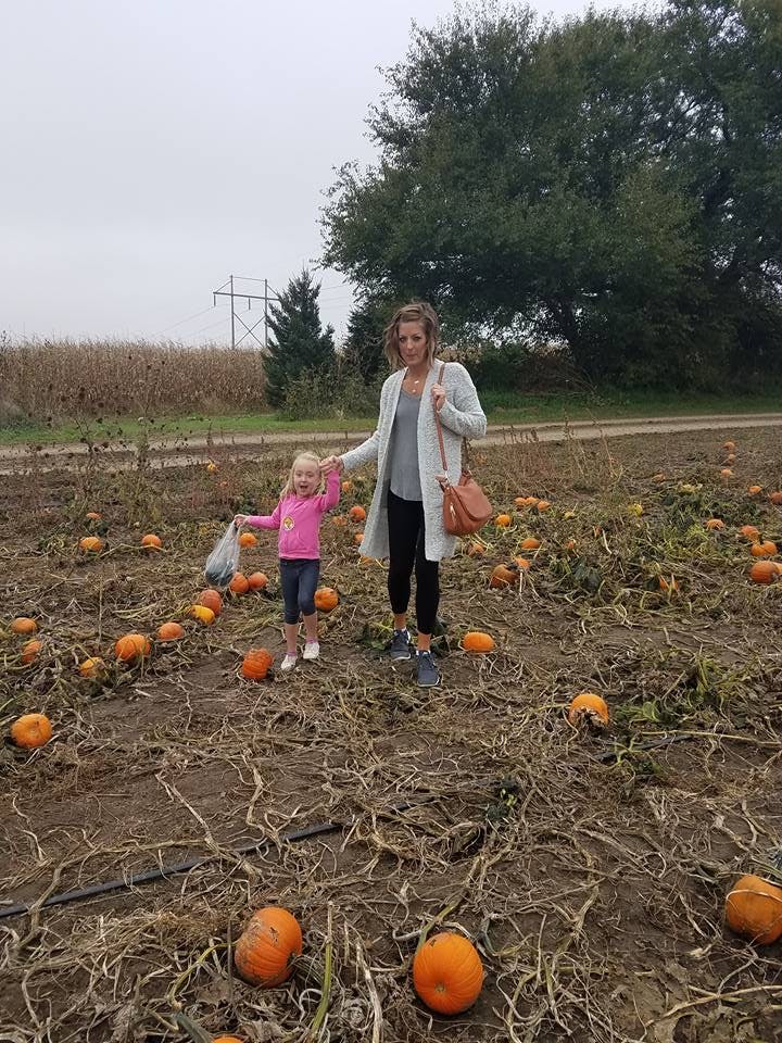 Person and child standing in a pumpkin patch