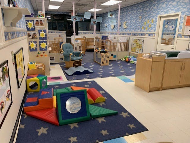 Childcare room with cribs, changing station, and colorful soft play shapes