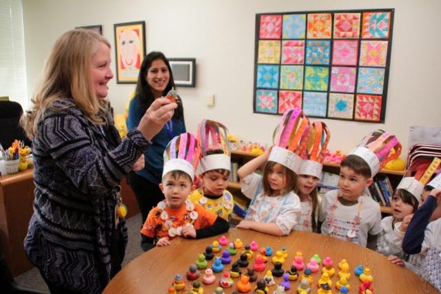 Adults and children wearing paper crowns around a table with small toys