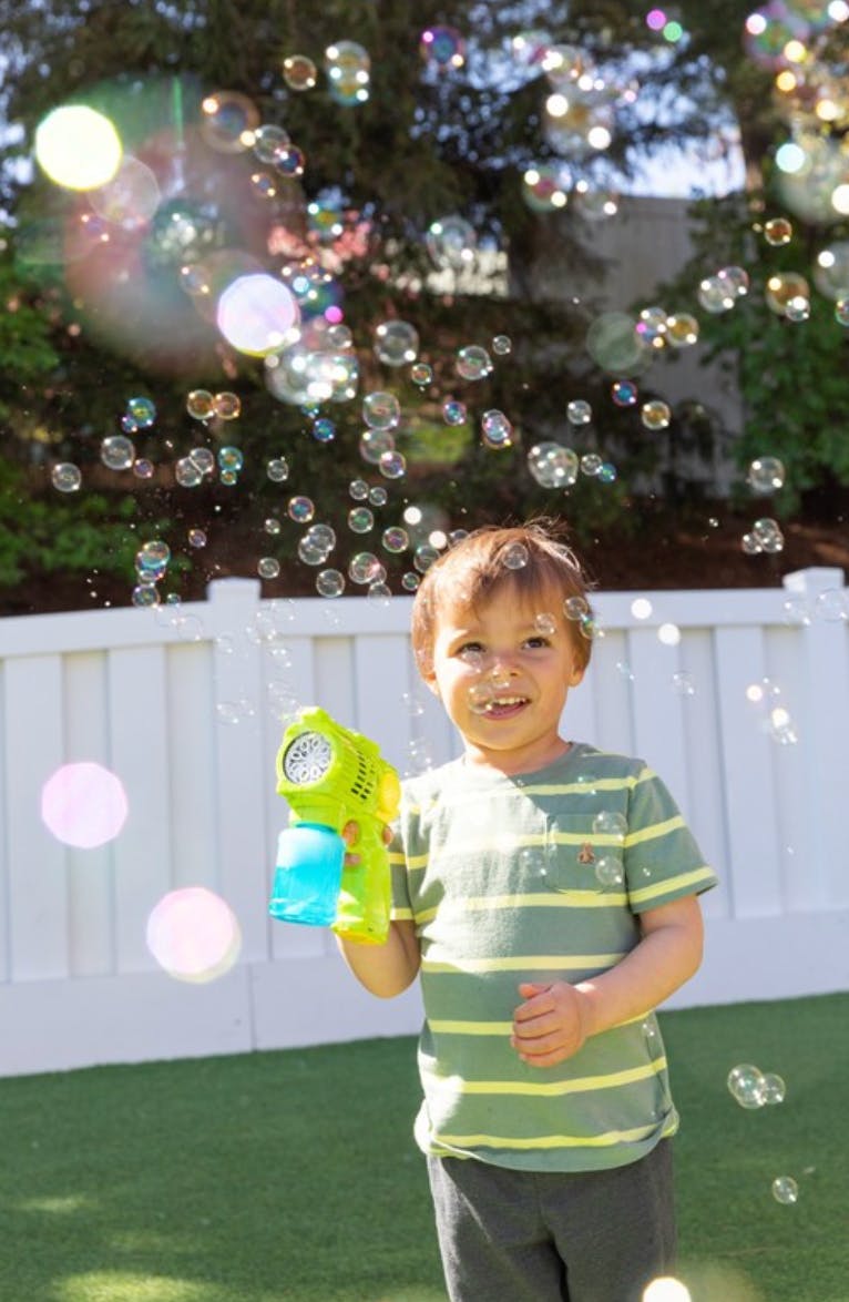 Child playing with a bubble gun surrounded by bubbles outdoors