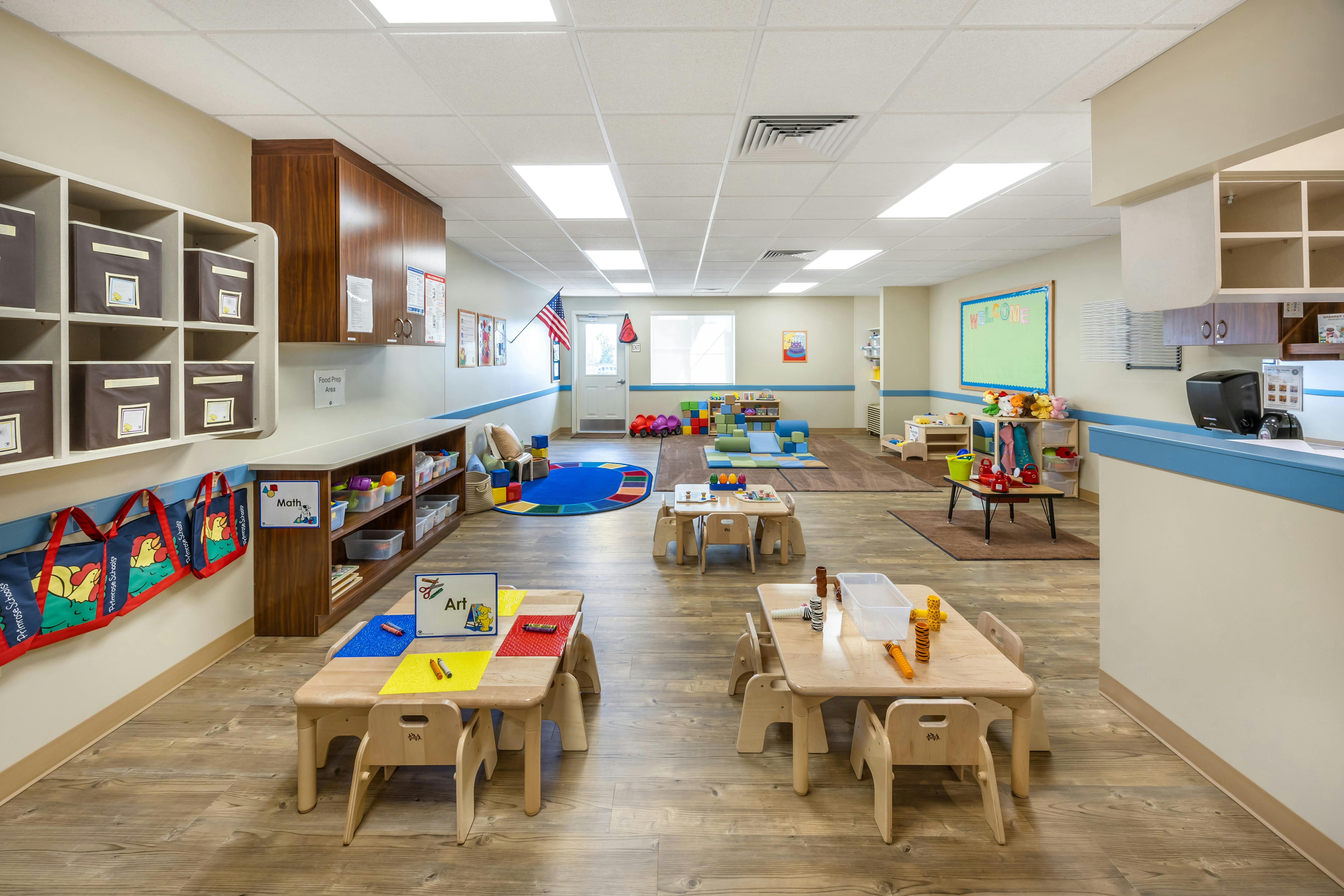 Classroom with small tables and chairs, play mats, and storage shelves