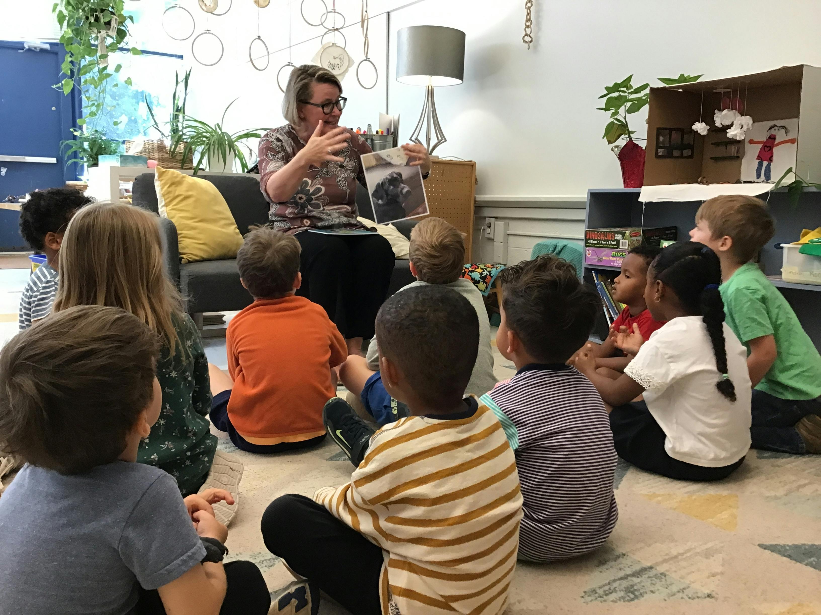 Person reading a book to a group of children sitting on the floor